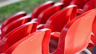 A row of red stadium seats, blurred in the background with green grass, close-up view.