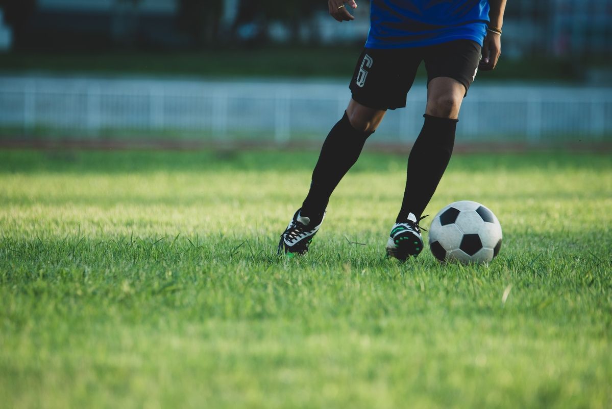 Ein Fußballspieler in einem blauen Trikot und schwarzen Shorts bereitet sich darauf vor, einen Fußball auf einem Rasenfeld zu schießen.