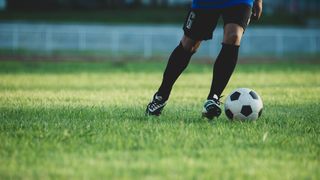 Ein Fußballspieler in einem blauen Trikot und schwarzen Shorts bereitet sich darauf vor, einen Fußball auf einem Rasenfeld zu schießen.