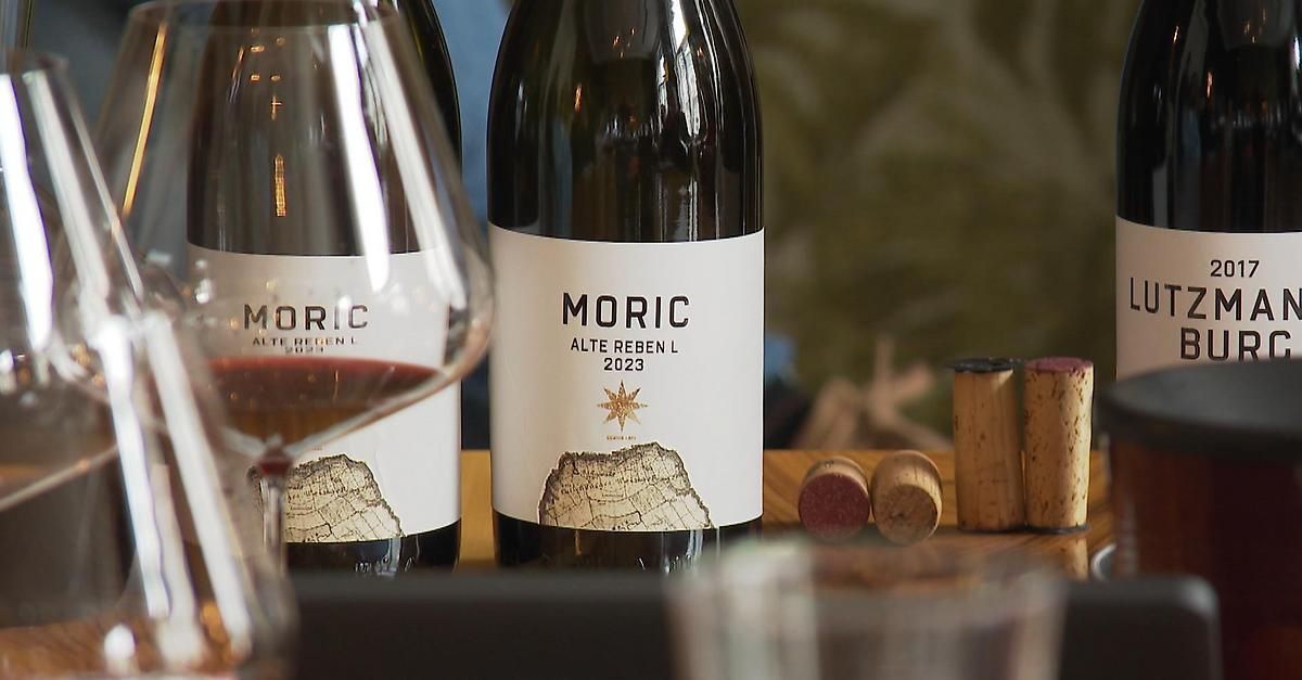 Two wine bottles labeled 'Moric Alte Reben L' are on a wooden table. One bottle is open, with wine in a glass. The other is sealed with corks.