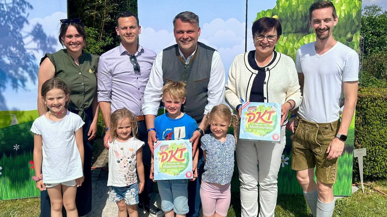 Eine Familie und zwei Erwachsene mit Kindern posieren vor einem Zeichentrickhintergrund und halten DKI-Boxen in der Hand.