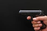 Eine Person hält eine schwarze Pistole mit dunklem Hintergrund. Die Waffe hat einen metallischen Finish und einen Sicherheitshebel.