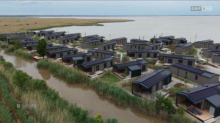An aerial view of a community of modern homes built near a lake and river, all with solar panels on the roofs.
