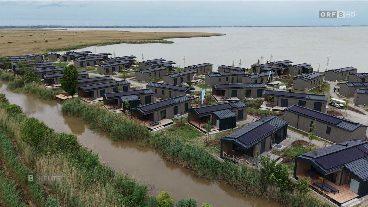 An aerial view of a community of modern homes built near a lake and river, all with solar panels on the roofs.