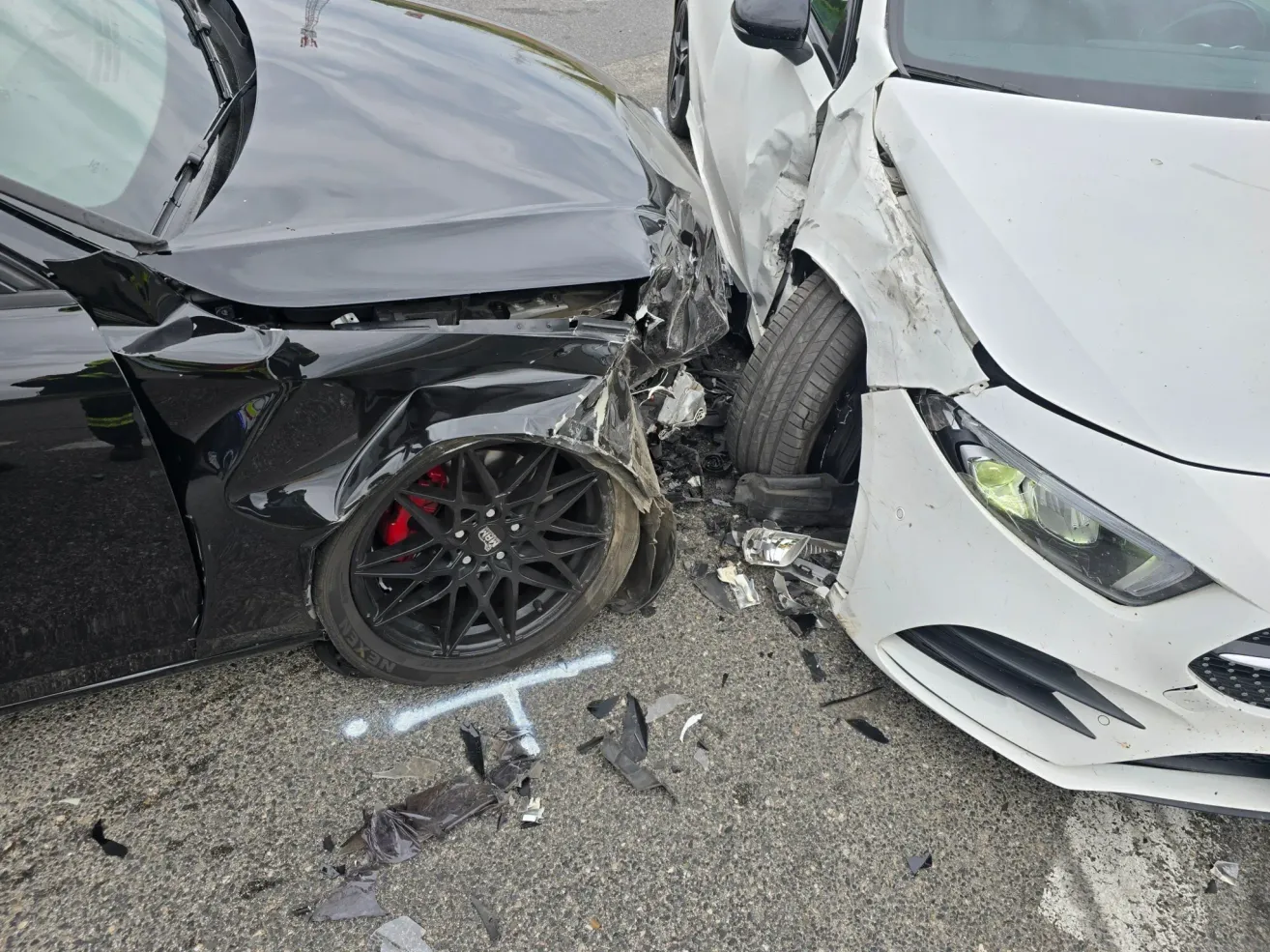 A black car and a white car are involved in an accident with damaged bumpers and broken glass. The black car has a damaged wheel.