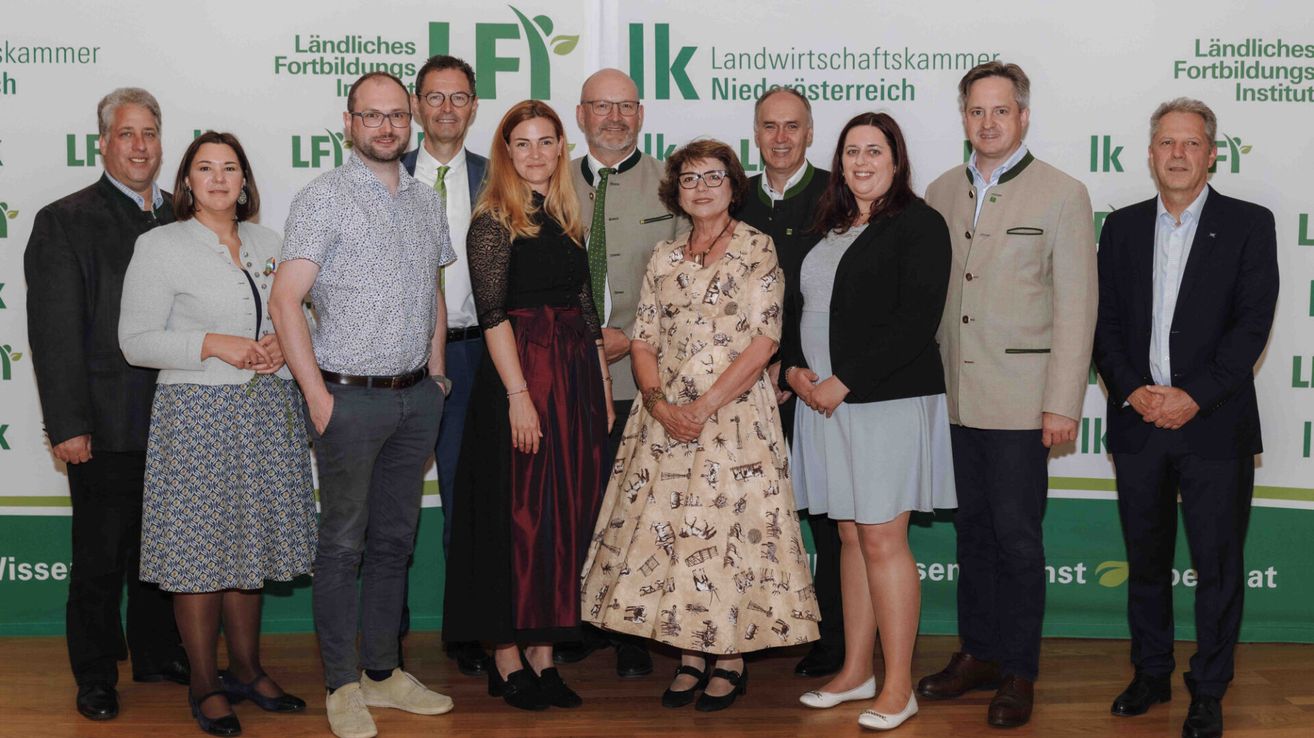 A group of people stands in front of a green and white banner, likely at an event. The individuals, dressed formally, seem to be posing for a photograph. The banner reads 'Landwirtschaftliche Landwirtschaftskammer Niederästerreich'.