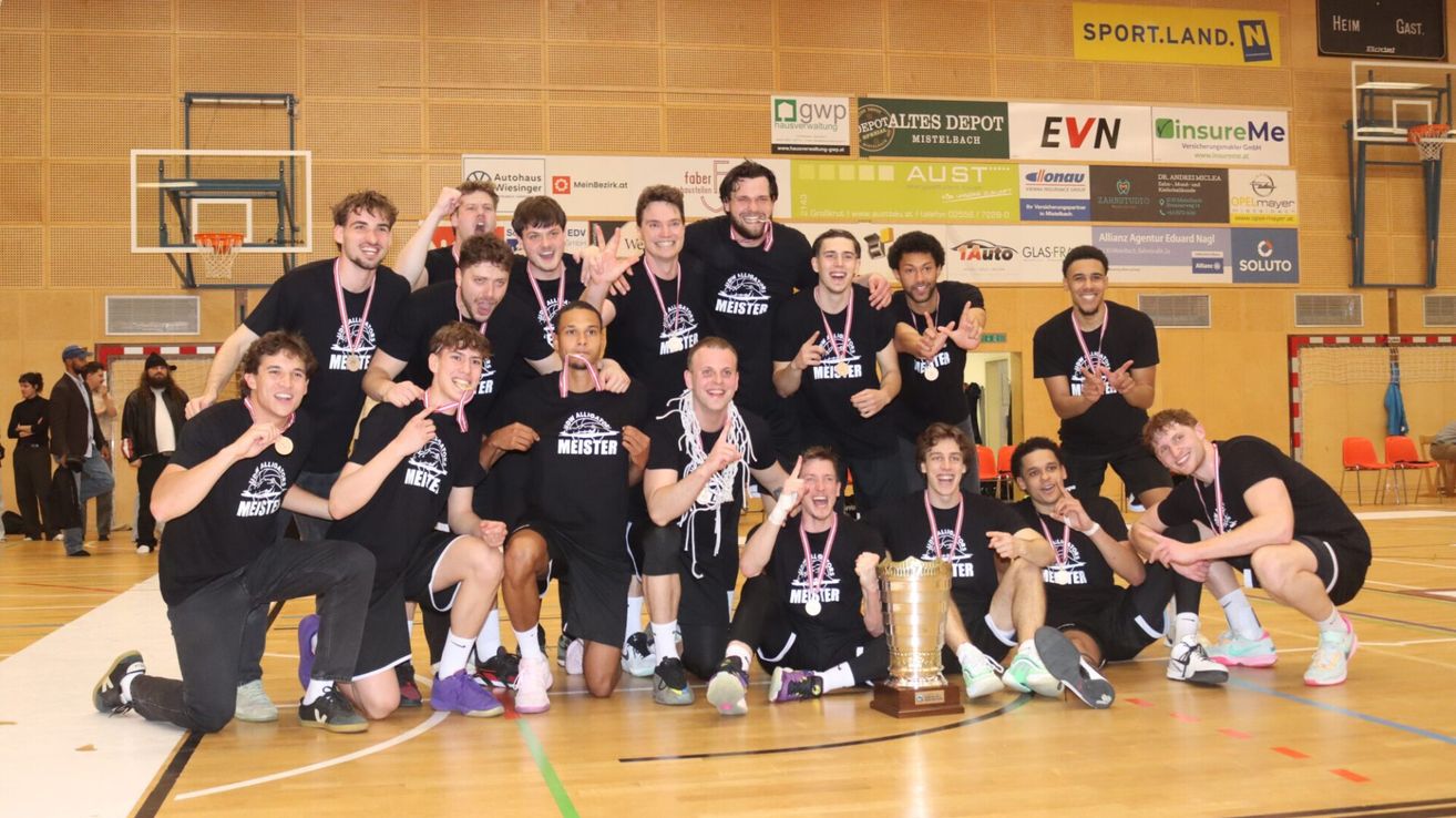 Eine Basketballmannschaft in schwarzen Shirts mit Meister darauf posiert mit einem Pokal für ein Foto.