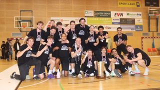 Eine Basketballmannschaft in schwarzen Shirts mit Meister darauf posiert mit einem Pokal für ein Foto.