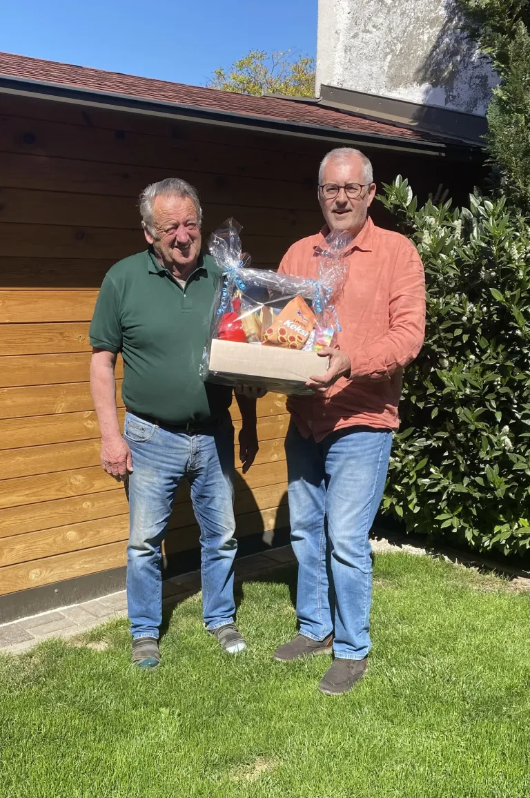 Two men stand on grass, one holding a box of snacks, smiling and posing for a photo.
