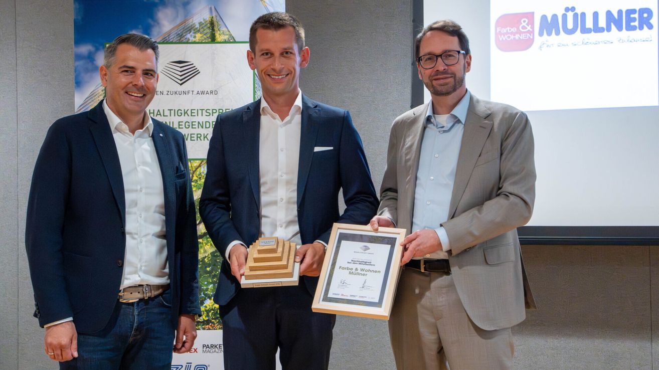 Three men stand together holding awards. One holds a plaque and another a small stack of wooden blocks. They smile and seem to be at an award ceremony.