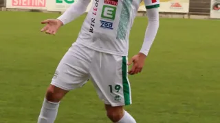 Ein Fußballspieler in einem weißen und grünen Trikot steht auf einem Feld, bereit einen Fußball zu treten.