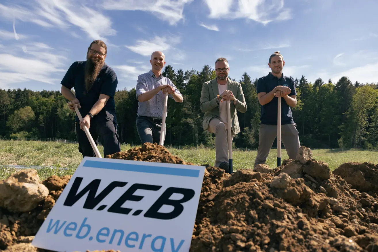 Four men with shovels pose for a photo in a field with a sign that reads W.E.B. web.energie.