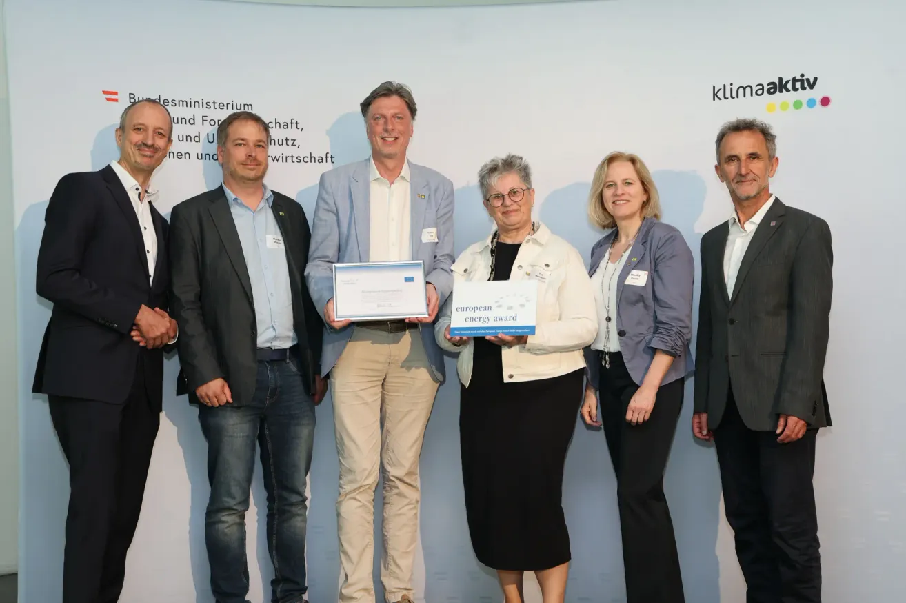 Fünf Personen posieren mit Urkunden in der Hand für ein Foto. Sie stehen vor einer Wand mit fremdsprachigem Text.