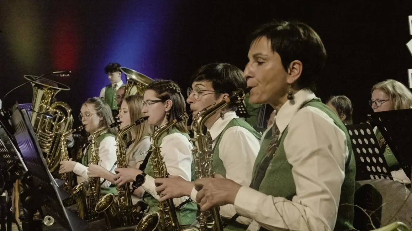 Eine Gruppe von Musikern spielt auf der Bühne und spielt Saxophon und andere Instrumente. Sie sind in passenden grünen Westen gekleidet.