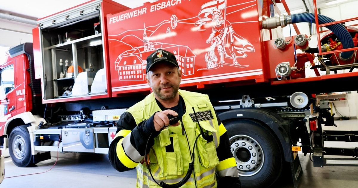 Ein Mann in einer reflektierenden Weste hält ein Funkgerät vor einem Feuerwehrauto.