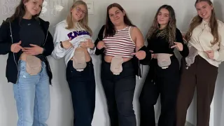 Fünf Frauen stehen in einem Raum, jede mit einem Prothesenbauch. Sie scheinen für ein Foto zu posieren. Hinter ihnen ist eine Tafel und eine Wand zu sehen.