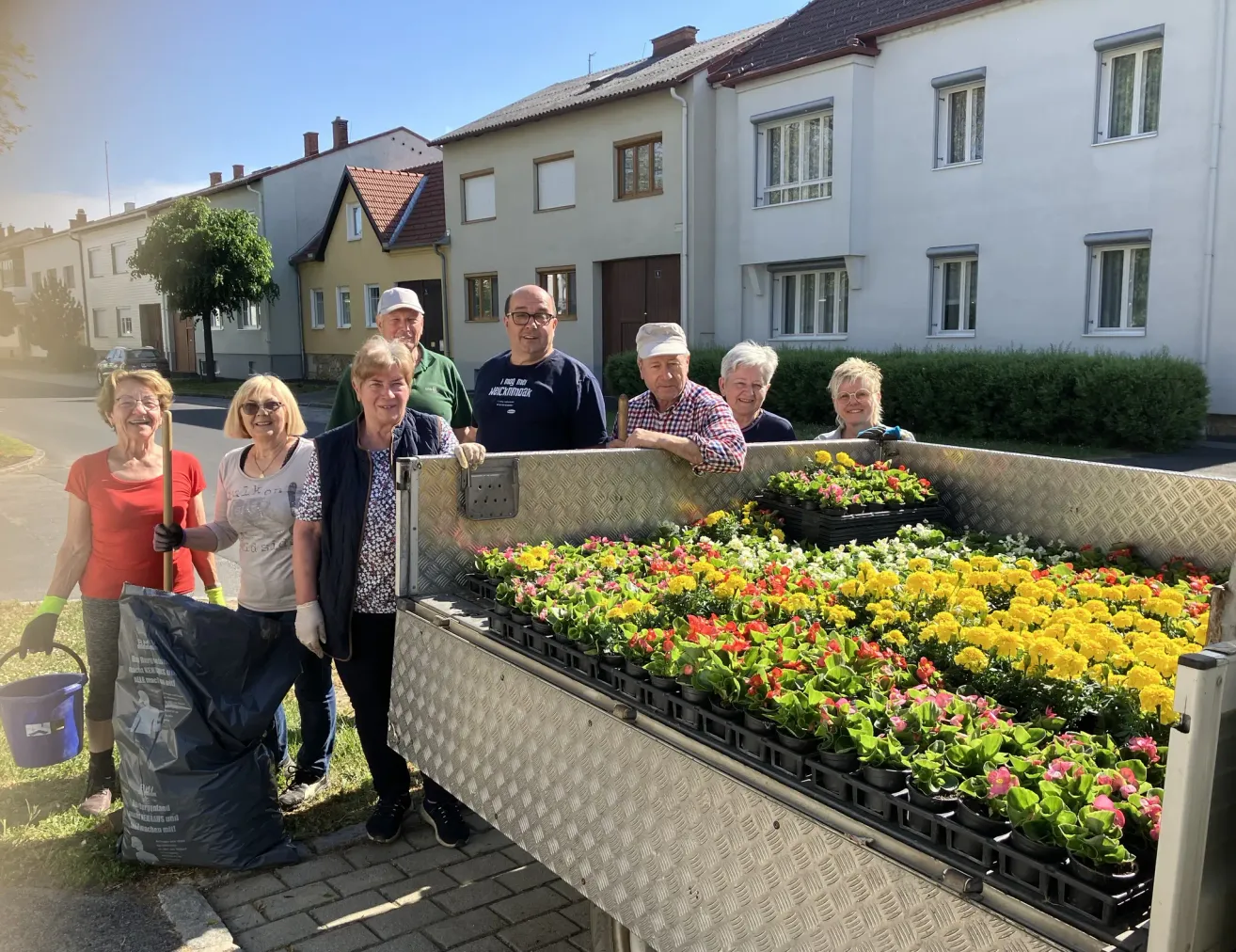 Eine Gruppe von Menschen steht neben einem mit Blumentöpfen gefüllten Lastwagen vor Häusern.