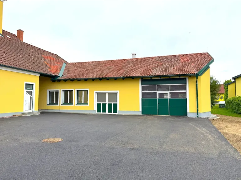 A yellow building with a red roof and green doors and windows, possibly a factory or commercial space, set in an open area.