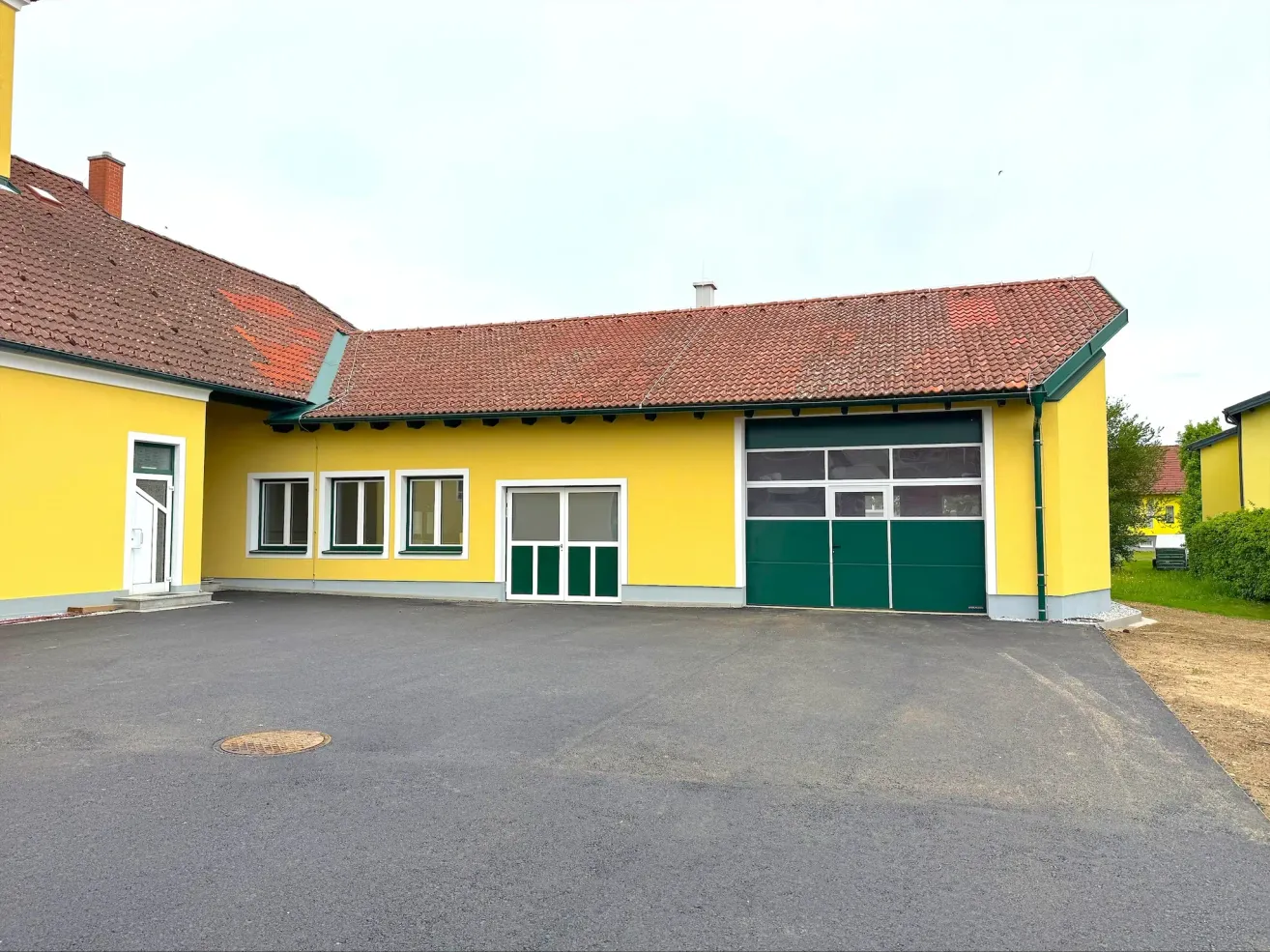 A yellow building with a red roof and green doors and windows, possibly a factory or commercial space, set in an open area.