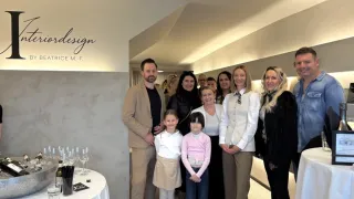 Eine Gruppe von Menschen, einschließlich Erwachsener und Kindern, steht in einem Raum mit weißem Hintergrund. Sie scheinen für ein Foto zu posieren, möglicherweise bei einer Veranstaltung.