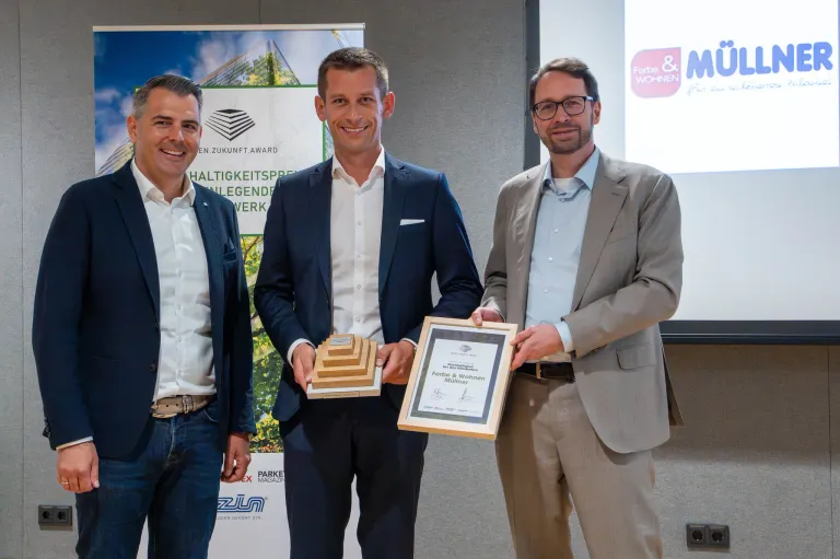 Three men are posing for a photo holding an award. The man in the middle is wearing glasses. They are standing next to each other.