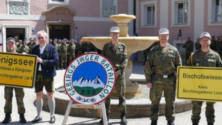 Four men in military uniforms stand in front of a fountain with a sign reading 'Gebirgsjager Battalion 232'. They hold signs that say 'Konigssee' and 'Bisschofswiese'.