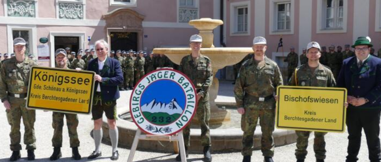 Four men in military uniforms stand in front of a fountain with a sign reading 'Gebirgsjager Battalion 232'. They hold signs that say 'Konigssee' and 'Bisschofswiese'.
