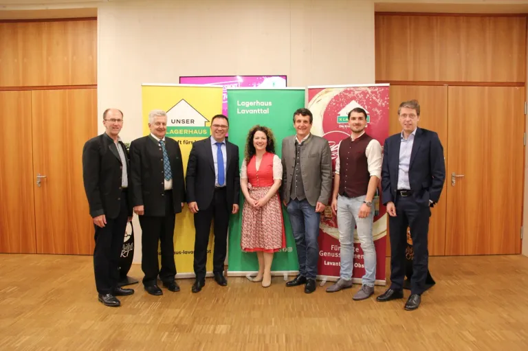 Eine Gruppe von Menschen steht vor Bannern für eine Lagerhaus-Veranstaltung, lächelt und posiert für ein Foto.