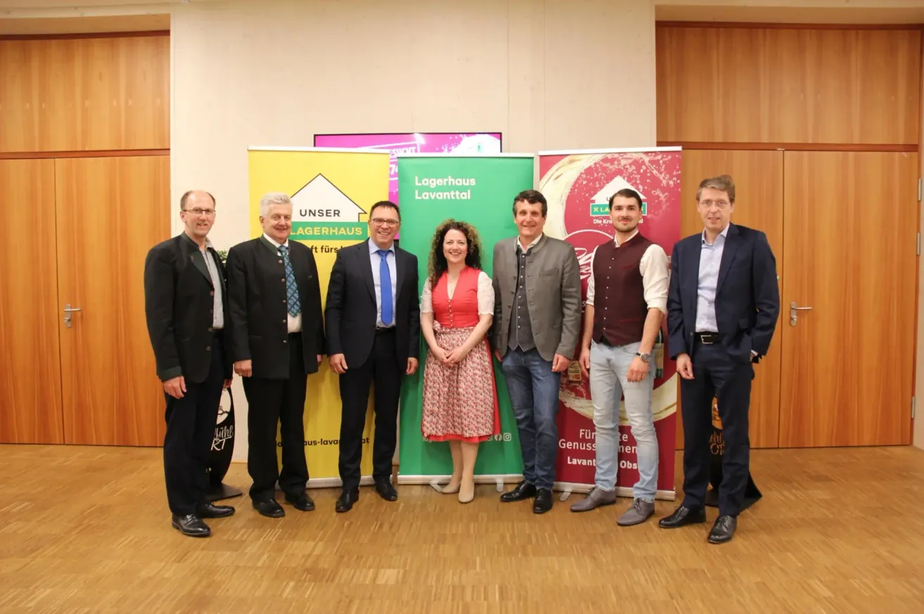 Eine Gruppe von Menschen steht vor Bannern für eine Lagerhaus-Veranstaltung, lächelt und posiert für ein Foto.