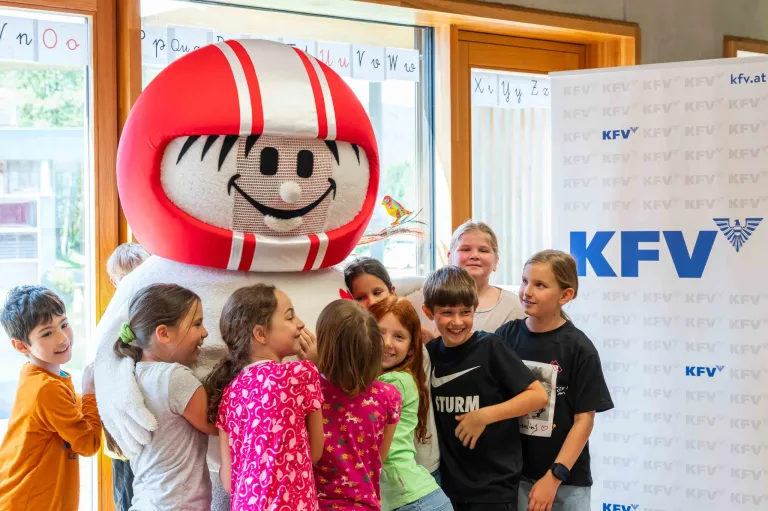 A group of children are posing for a photo with a large mascot dressed in a red and white football uniform.