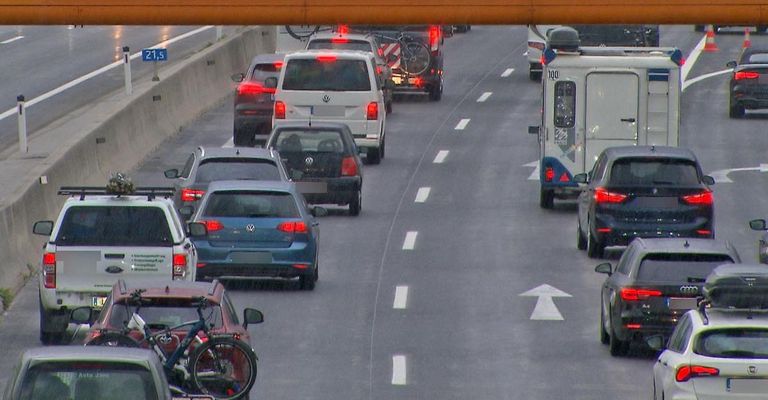 A busy highway with multiple cars and a van, some with bicycles on their roofs. White lines mark lanes and arrows indicate traffic direction.