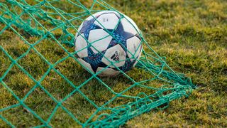 A soccer ball with a blue and white design is stuck in the net on a grassy field.