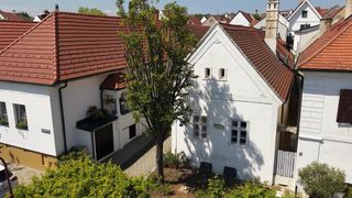 A top-down view of a neighborhood with houses, a small tree in the center, and a brick walkway. The houses have brown roofs and white walls.