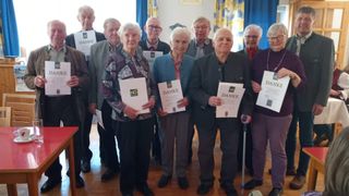 A group of elderly people are standing together holding certificates that say Danke. They are all smiling for the photo.