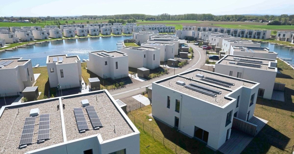 Aerial view of a modern housing estate with many houses, a lake, and solar panels on the roofs.