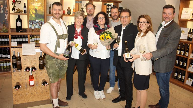Eine Gruppe von Menschen posiert für ein Foto in einem Weinkeller mit Weinflaschen und Gläsern in der Hand.
