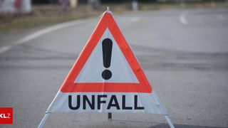 A traffic sign on the side of the road with the word Unfall written on it. It is an orange and white triangle with a black exclamation mark.
