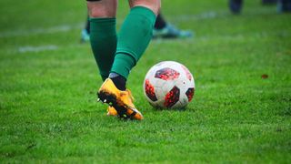 A soccer player wearing green socks is kicking a soccer ball on a green field.