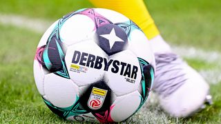 A Derbystar soccer ball, the official match ball of Bundesliga, lies on the grass with a player's foot nearby.