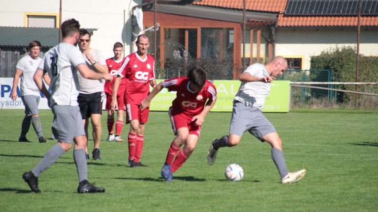 Eine Gruppe von Fußballspielern in roten Trikots spielt auf einem Rasen. Ein Spieler versucht, den Ball zu treten, während ein anderer Spieler verteidigt.