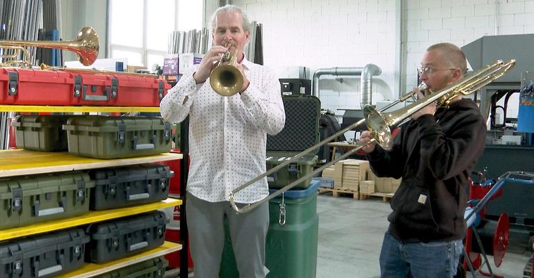 Zwei Männer in einem Lager spielen Musikinstrumente, einer spielt Trompete und der andere Posaune.