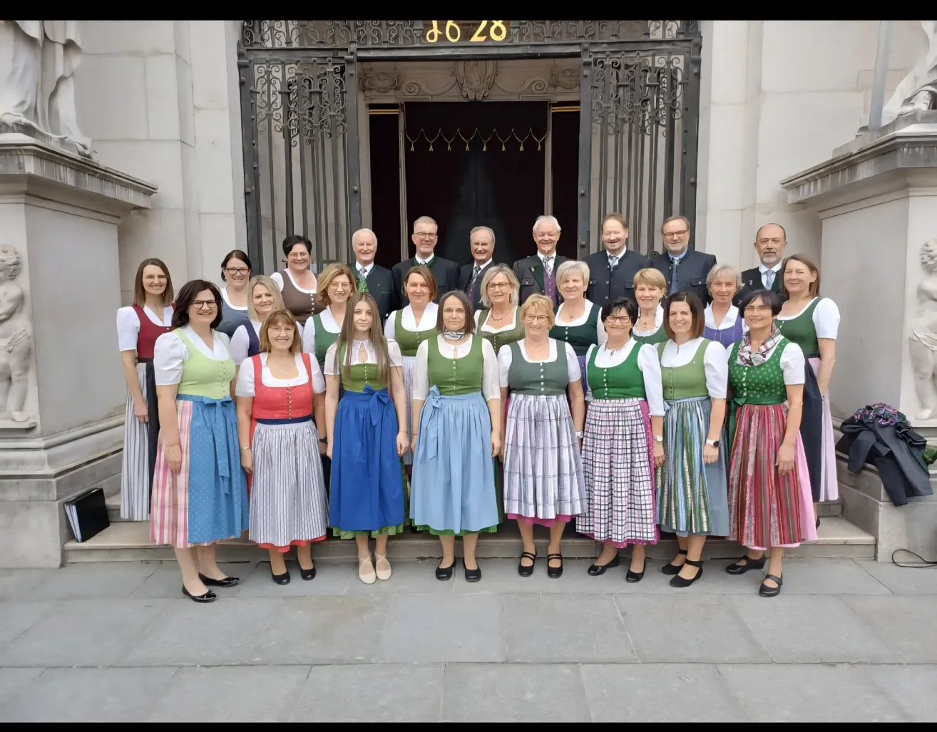 Eine Gruppe von Menschen in traditionellen Kleidungsstücken steht vor einem Gebäude. Sie posieren für ein Foto.