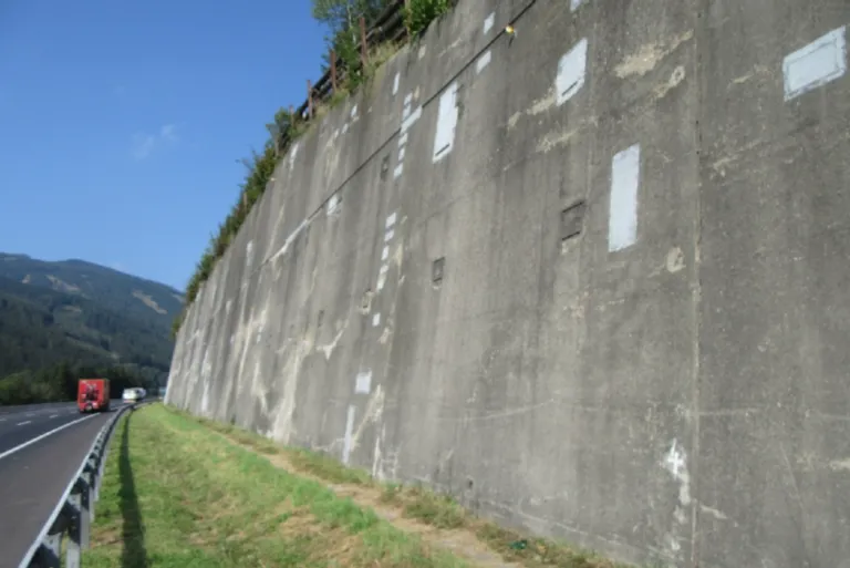 A concrete wall with a few white rectangular areas and a small grass patch at the base.