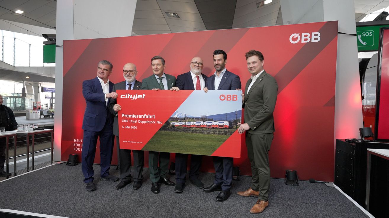 A group of men in suits stands behind a large poster with the text Cityjet. They are smiling and posing for a photo.
