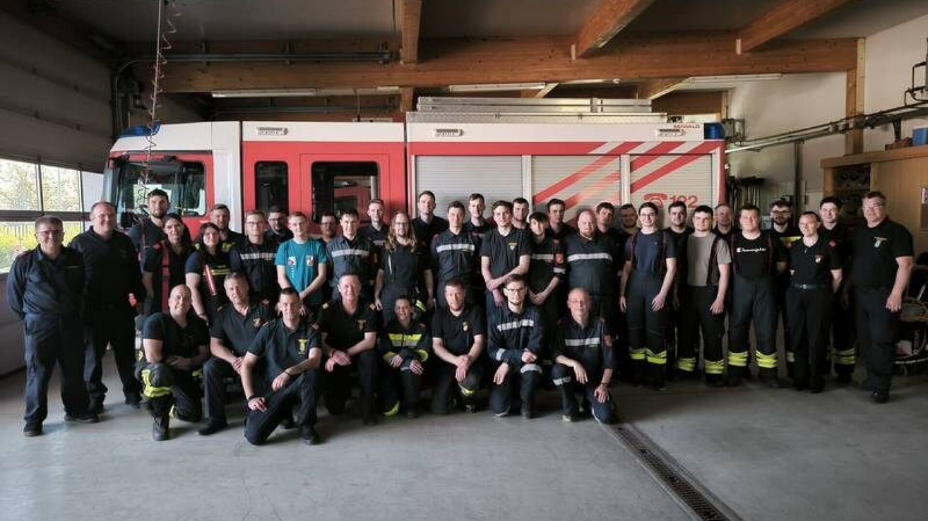 Gruppenfoto von Feuerwehrleuten in einer Feuerwache mit einem Feuerwehrauto im Hintergrund.