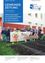 Eine Gruppe von Kindern und Erwachsenen steht in einem Garten mit einem Banner. Das Banner hat eine Karotte und der Text lautet GemuseAckerdemie. Sie halten eine Gießkanne und ein Schild.