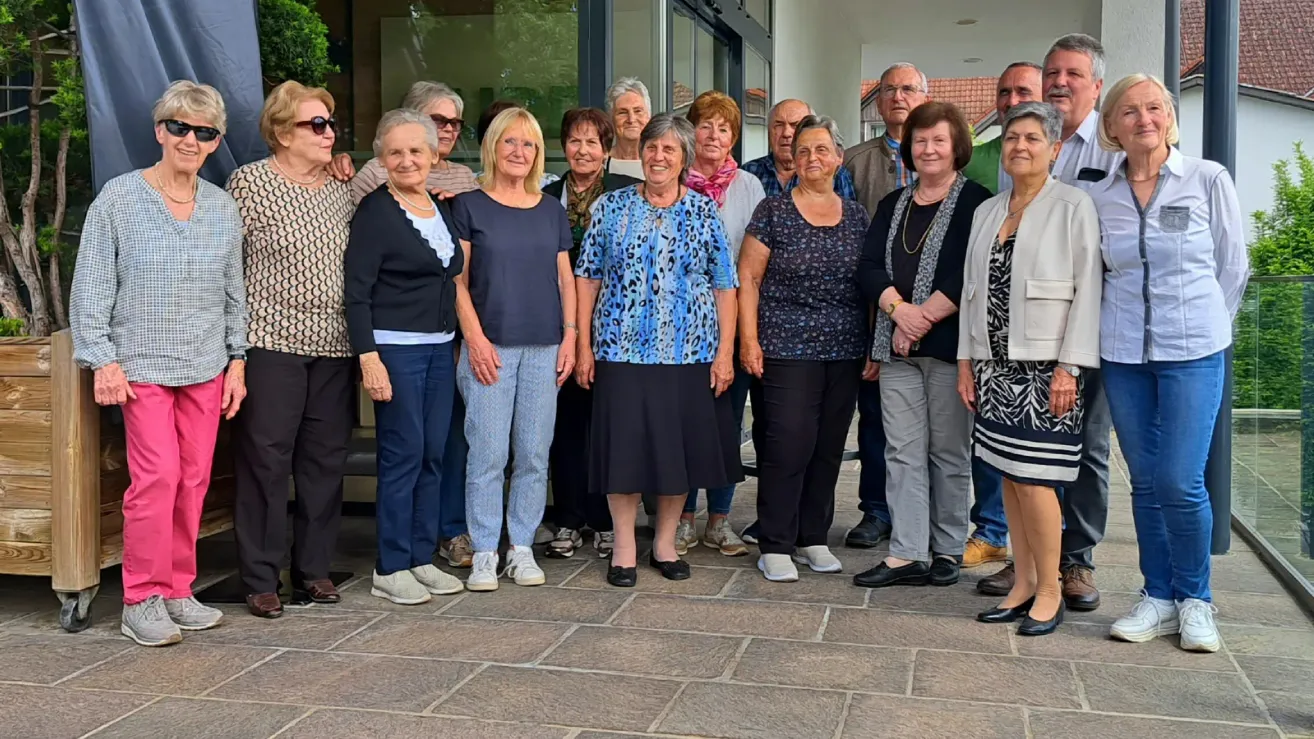 A group of people, predominantly older adults, are posing for a picture outside a building. They are dressed casually and appear to be smiling.