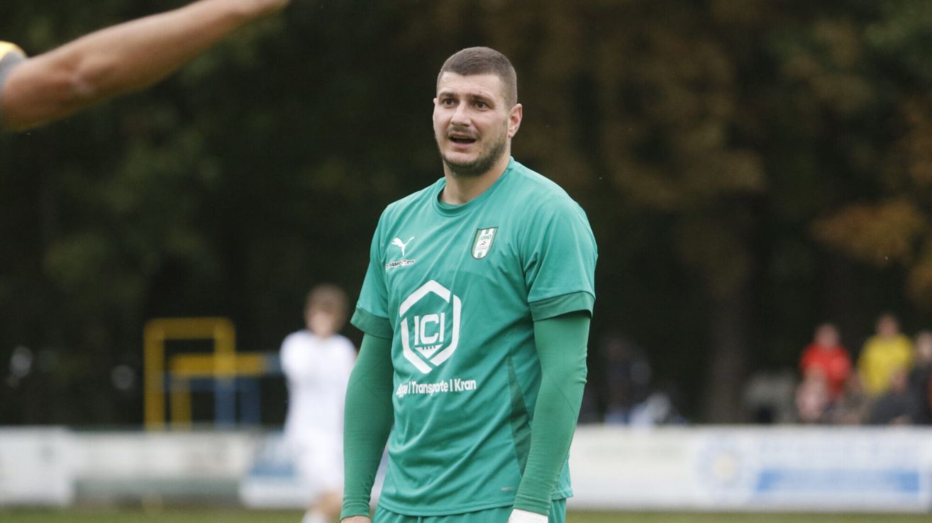 Ein Fußballspieler in einem grünen Trikot steht auf einem Feld, wahrscheinlich während eines Spiels oder Trainings.