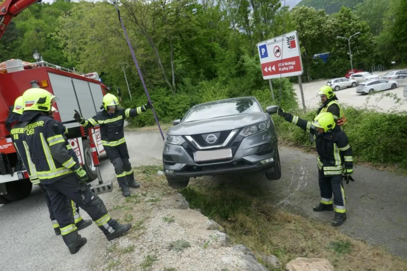 Firefighters use ropes to pull a car stuck on the side of a road. A sign behind them reads 275 m Wildbad.