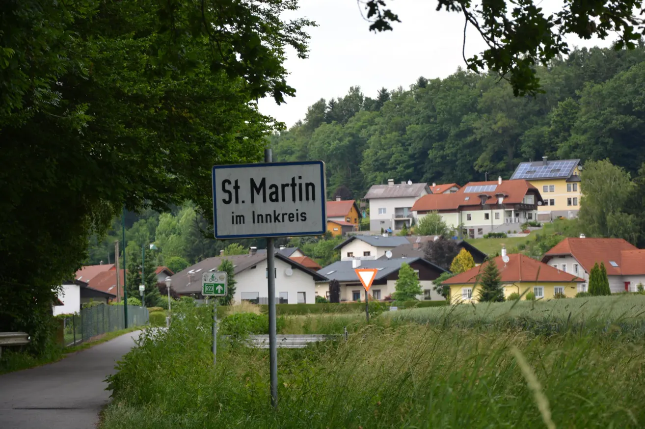 Ein Straßenschild für St. Martin im Innkreis, Österreich. Das Gebiet ist von Häusern mit Bäumen und Solarmodulen auf einigen Dächern umgeben.